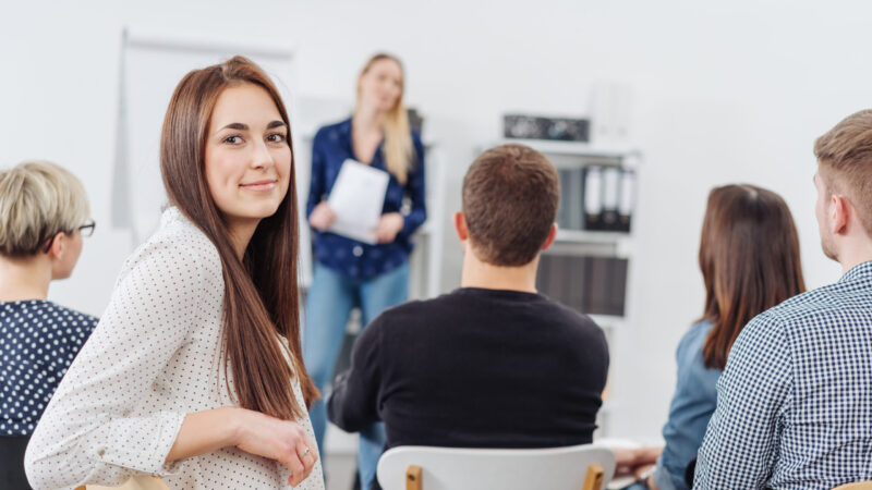 Young woman in a lecture turning to camera Young woman in a lecture or business presentation turning to smile at the camera viewed from the back of the room