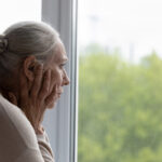 Ältere demente Frau schaut aus einem Fenster ins Grüne