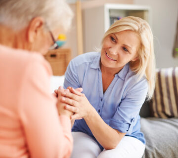 EinePflegerin spricht liebevollmit einer Seniorin