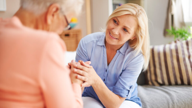 EinePflegerin spricht liebevollmit einer Seniorin