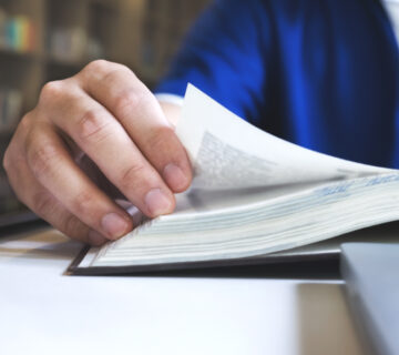 Ein Mann liest in einem Buch  Der Fokus ist auf seiner Hand, mit der er eine Seite umblättert 