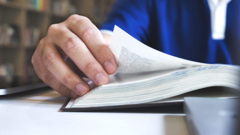 Man reading a book. Education, Academic, Learning and Exam conce Ein Mann liest in einem Buch. Der Fokus ist auf seiner Hand, mit der er eine Seite umblättert.