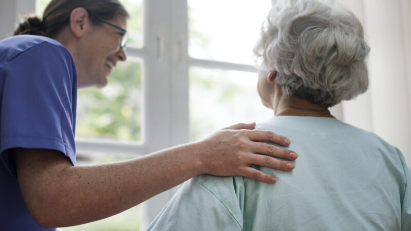 Nurse taking care of an old woman Lächelnde Pflegerin und eine alte Dame, die aus dem Fenster schaut