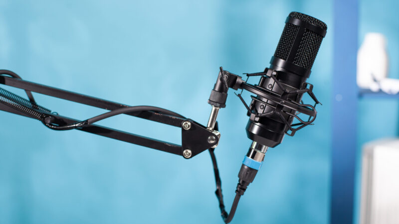 Closeup of professional microphone swivel boom arm stand in empty vlog broadcasting studio Mikrophon für einen Podcast vor blauem Hintergrund